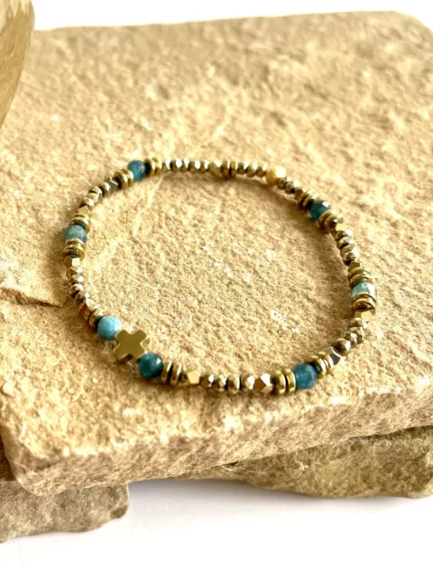 bracelet tiny cruz apatite est un bracelet très fin en hématites dorées, une croix centrale et des pierres apatite bleu canard