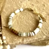 bracelet-nymphe-aigue-marine-pierres-fines-paulettequincaillerie-bijoux-créateur_30 bracelet nymphe aigue marine est un bracelet puka style surfeur chic en perles heishi en pierre d'aigues-marines marine à facettes et coquillages blanc avec une cartouche centrale en perles or