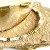 collier-nymphe-aigue-marine colier nymphe aigue marine est un collier puka style surfeur chic en coquillages blanc et perles heishi aigue marine à facettes et cartouche de perles centrales or